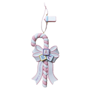 A baby shower Christmas ornament shaped like a candy cane with a pink and white striped handle, a matching bow, alphabet blocks spelling ABC, and a ribbon that reads 'Baby's 1st Christmas'.