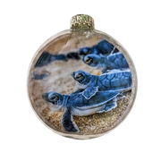 A round glass ornament featuring a printed or embedded photograph of sea turtle hatchlings on sand, with a gold cap at the top, shown against a plain white background.
