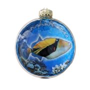 A round glass Christmas ornament featuring a colorful tropical fish illustration over a blue ocean background with coral, topped with a gold cap and hanging loop.