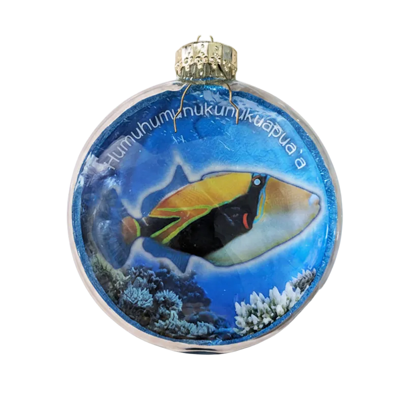 A round glass Christmas ornament featuring a colorful tropical fish illustration over a blue ocean background with coral, topped with a gold cap and hanging loop.