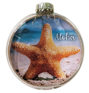 A round glass Christmas ornament featuring a printed beach scene with an orange starfish on sand and the word 'Aloha' in white script, topped with a silver cap.