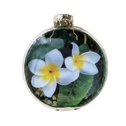 A round glass Christmas ornament featuring a printed tropical design of white plumeria flowers with yellow centers and green leaves, complete with a gold glittery cap and wire hanger.