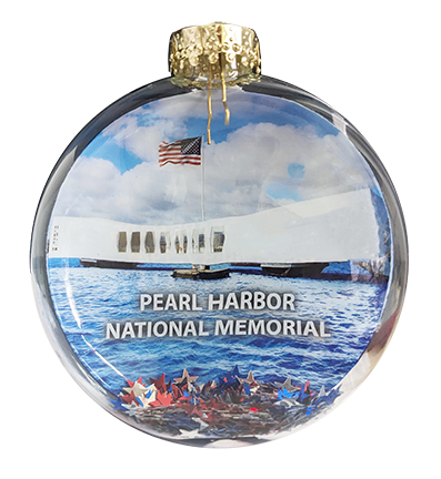 A round clear glass ornament featuring a printed image of the Pearl Harbor National Memorial, with blue sky and water, a white ship, an American flag, and a gold hanging cap at the top.