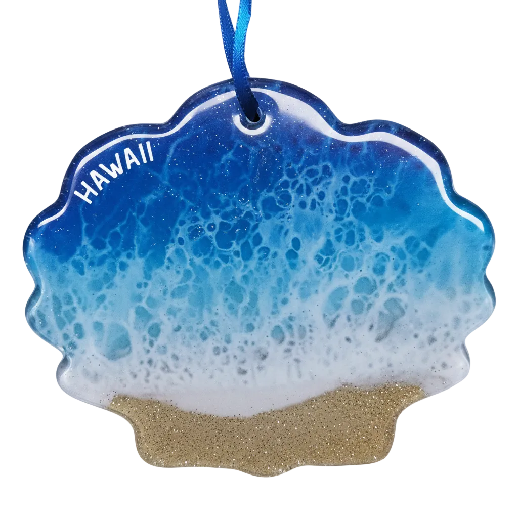 A scalloped shell-shaped ornament featuring a blue and white ocean wave pattern with white 'HAWAII' text and a glittery gold sand base, hanging from a blue ribbon on a white background.