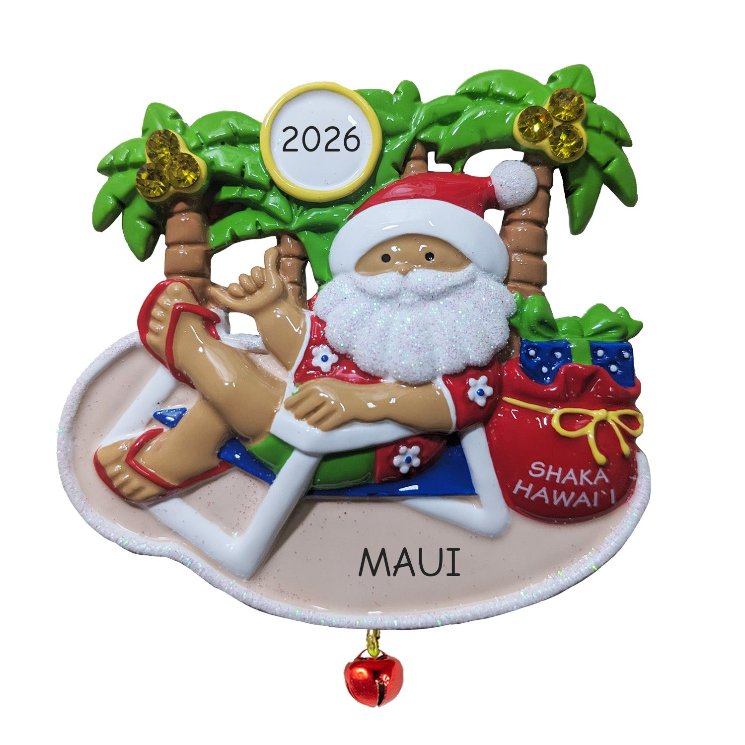 A white decorative sign shaped like the state of Hawaii, with cutout palm trees and printed text reading 'SHAKA Hawaiian Hand Gesture meaning "Hang Loose"' plus 'SANTA'S PEN® © JKC'. A small red bell hangs from the bottom center.