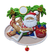 A Hawaiian Christmas ornament Santa Claus ornament lounging on a beach chair with palm trees and a 'Shaka Hawaii' bag.