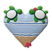 A Hawaiian Christmas Ornament of a heart-shaped ornament with two green sea turtles on a beach. 